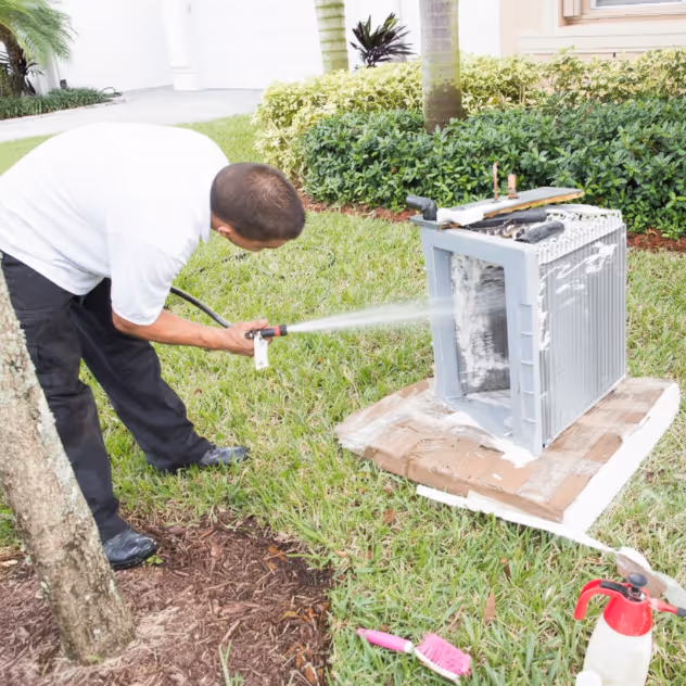 Floriduct technician rinsing the fins of an outdoor AC condenser coil with a hose