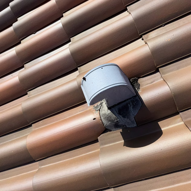 A metal dryer vent termination cap set into a barrel-tile roof on a South Florida home