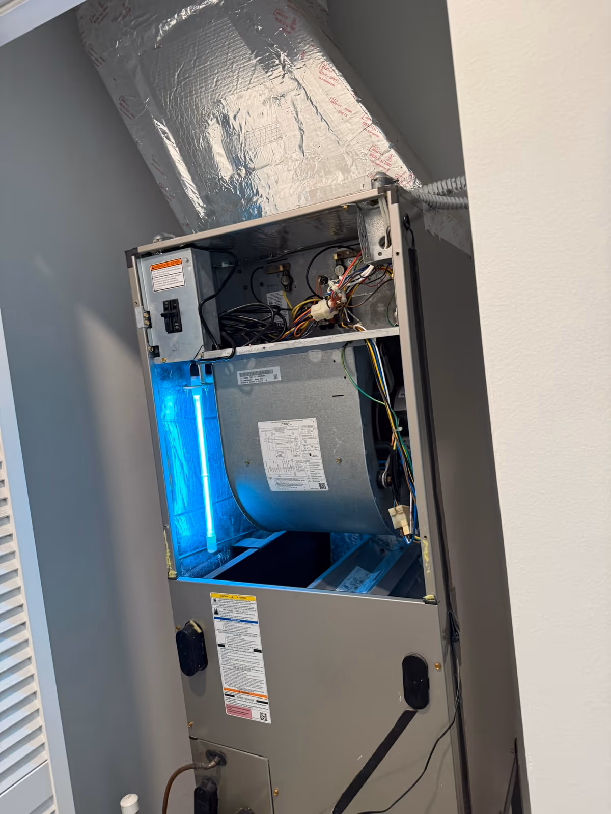 UV-C lamp glowing blue inside an open vertical air handler cabinet after installation, mounted beside the blower