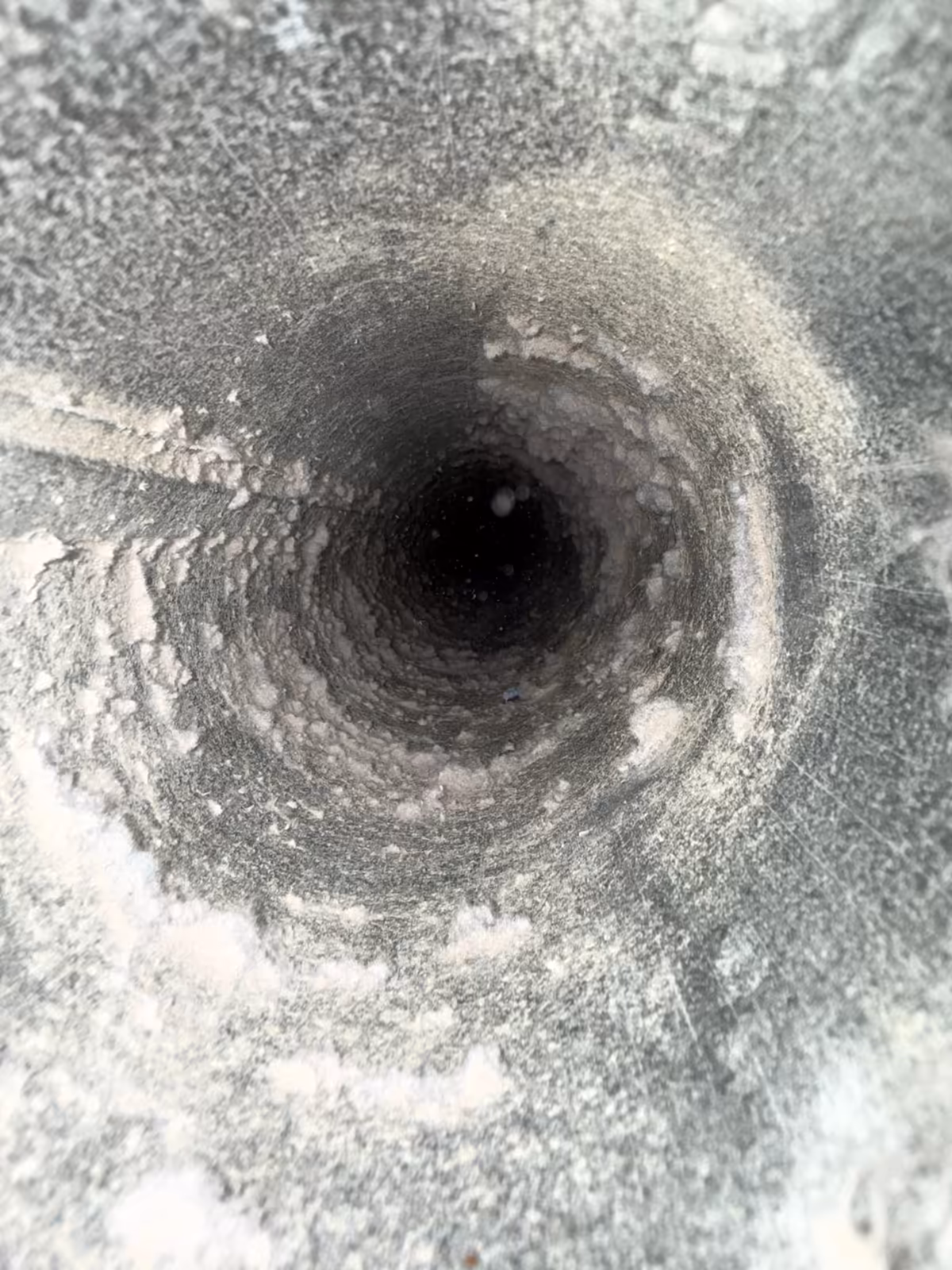 Looking down a round dryer vent pipe before cleaning, the metal coated in a layer of grey lint dust