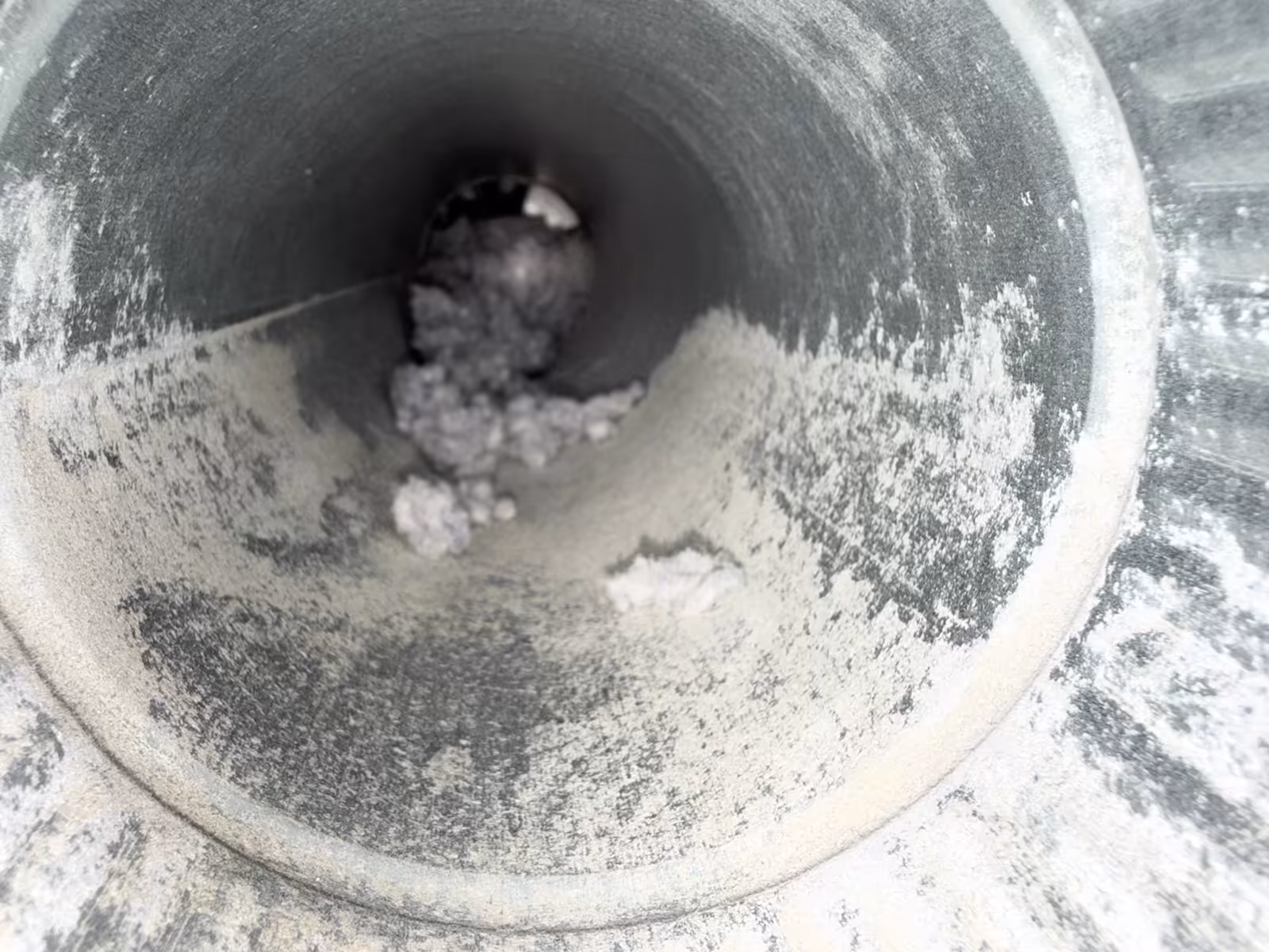 Inside the dryer vent pipe before cleaning, lint and grey dust coating the metal wall along the run