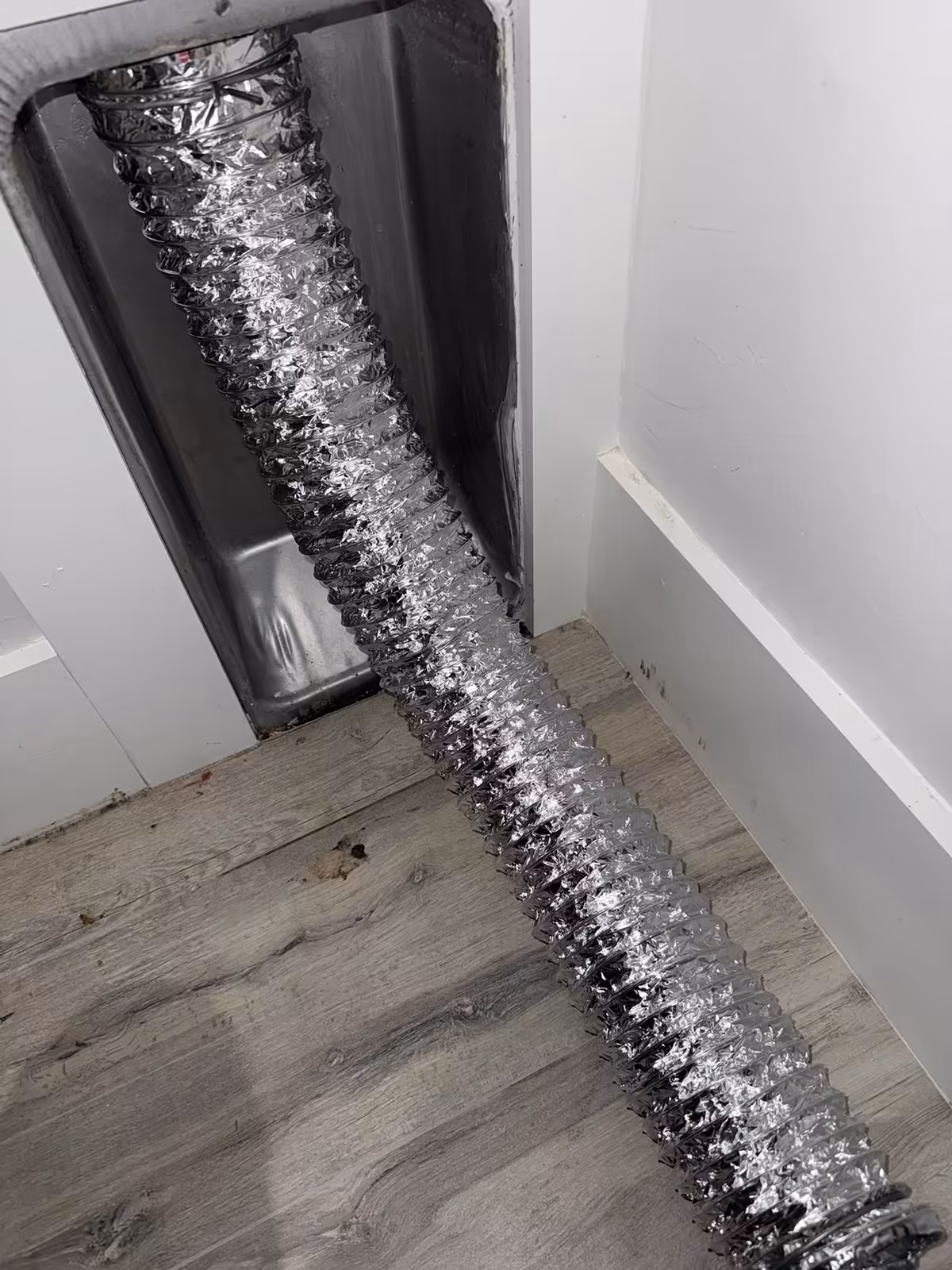 New foil dryer duct connected into the recessed wall vent box and run back along the laundry room floor