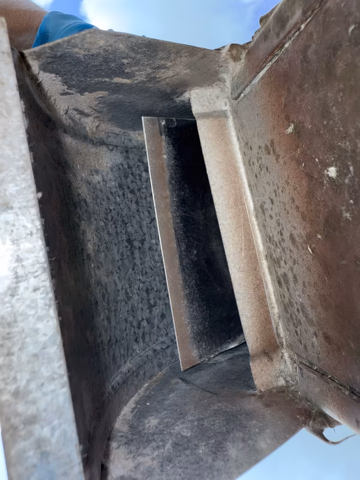 The same rooftop vent hood after cleaning, bare galvanized metal with the damper flap free to swing