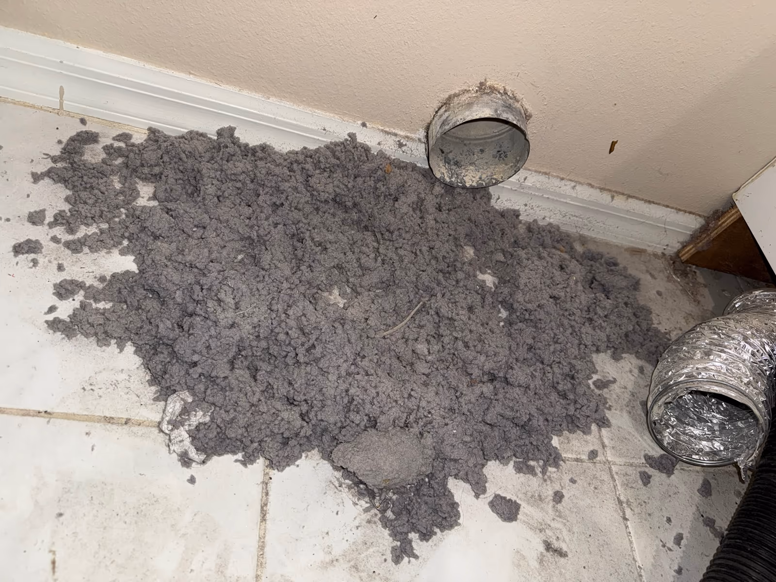 Lint cleared from a dryer vent duct opening and spread across a laundry room floor
