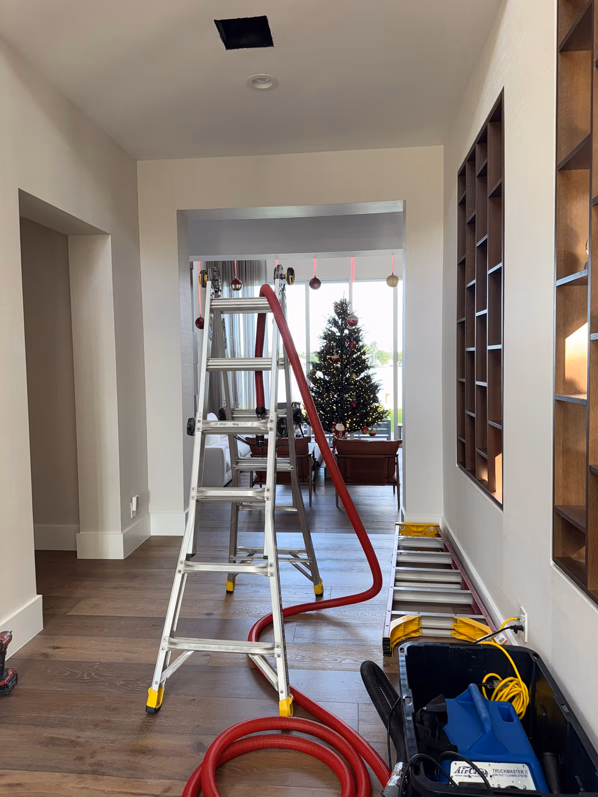 Floriduct duct-cleaning vacuum hose and ladder set up beneath an open ceiling vent during a home air duct cleaning