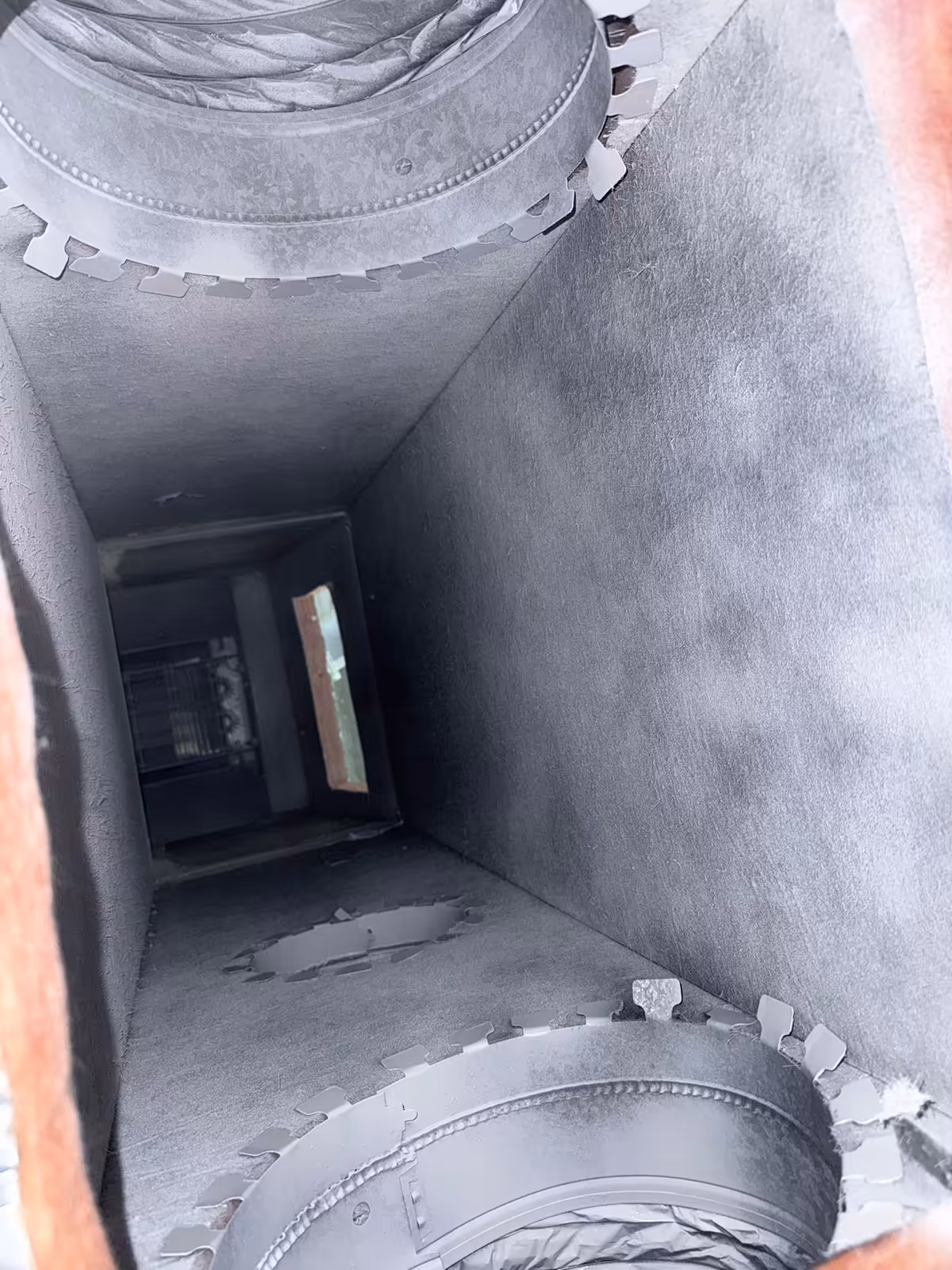 The same plenum after cleaning, the grey duct board lining clear and two round takeoff collars with flexible duct attached top and bottom