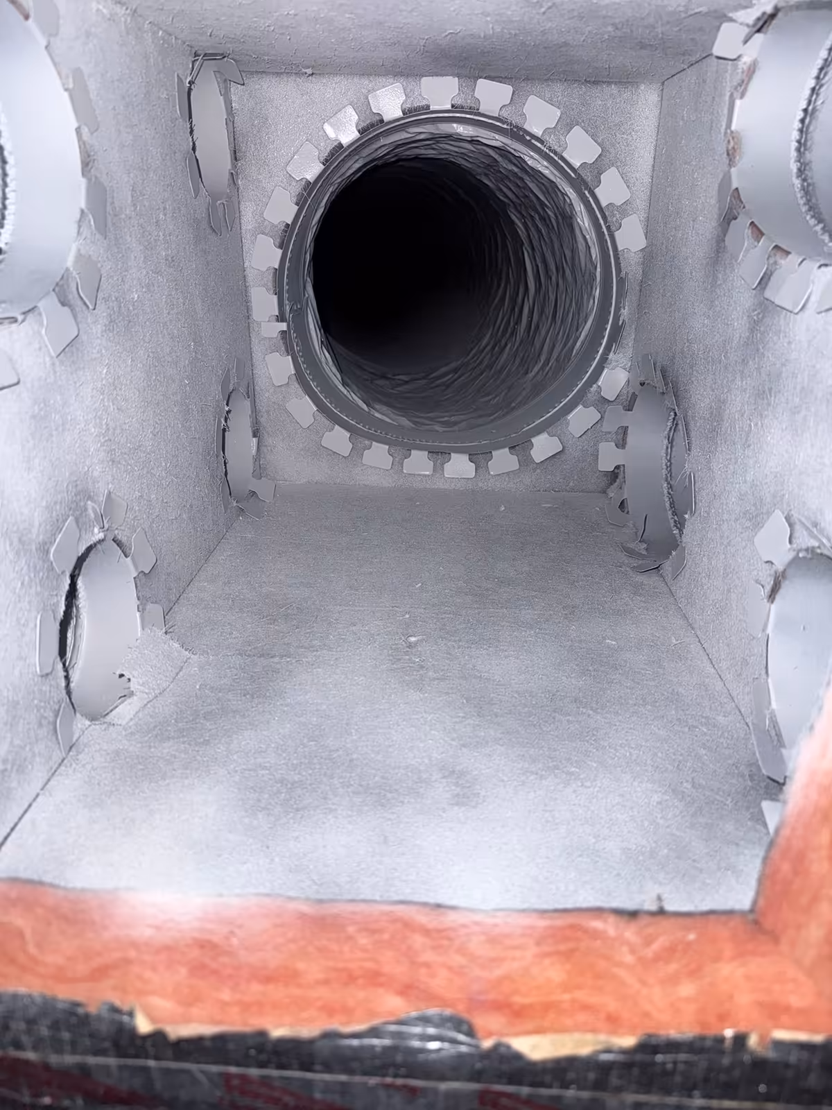 The same duct box after cleaning, the walls, floor and round flexible takeoff clear of dust, with the orange fiberglass batt visible at the cut edge